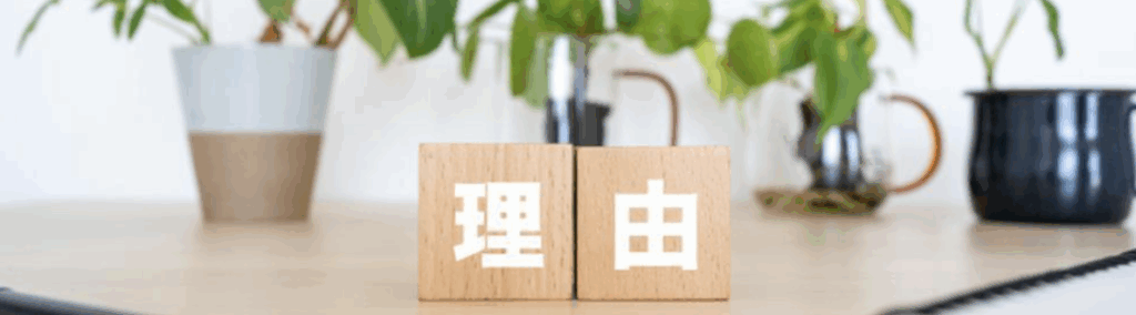 観葉植物が並ぶ机の上に置かれた『理由』の文字ブロック、背景にペンとノート